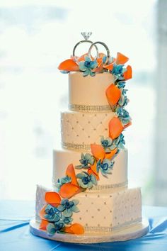 a three tiered wedding cake with orange and blue flowers