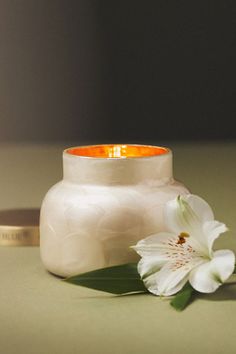 a white vase sitting on top of a table next to a flower and a candle