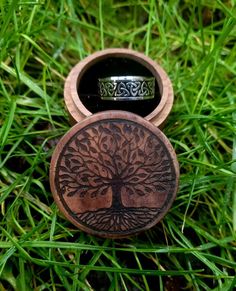 a wooden ring box with a tree on it sitting in the middle of some grass