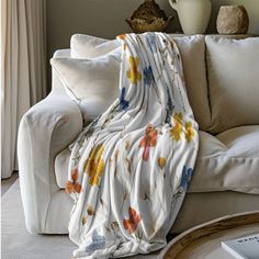 a white couch with a blanket on top of it next to a coffee table and vase