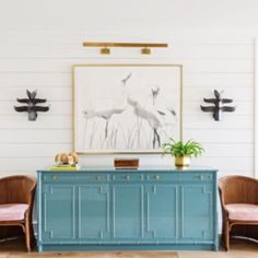 two chairs are sitting in front of a blue cabinet with artwork on the wall behind it