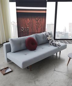 a blue couch sitting in front of a window next to a table with a red pillow on it