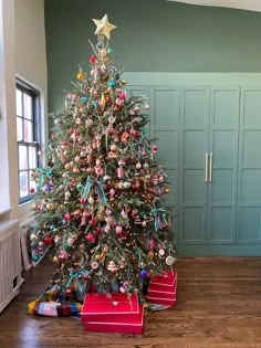 a decorated christmas tree in a room with green walls and wooden floors, along with red boxes on the floor