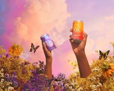 two hands holding up cans of food in front of flowers and butterflies flying around them