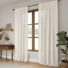 a living room with white curtains and a wooden table in front of the window that has a potted plant next to it