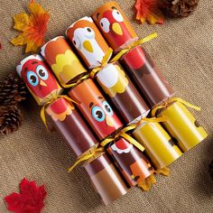 several colorful candles are wrapped in brown paper and tied with yellow ribbon, sitting on a table next to autumn leaves