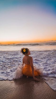 a woman in an orange dress sitting on the beach