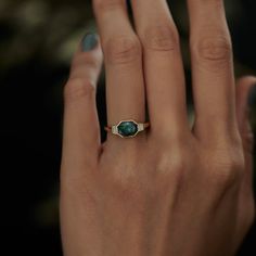 a woman's hand with a gold ring and green stone on her left hand