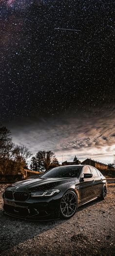 a black car parked on the side of a road under a night sky filled with stars