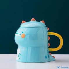 a blue ceramic mug with a yellow handle and an animal face on the side, sitting on a white surface