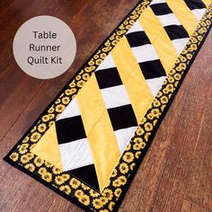 the table runner quilt kit is laying on top of a wooden floor with yellow and black stripes