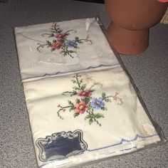 two white handkerchiefs with flowers on them sitting next to a brown potted plant