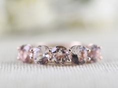 three stone ring sitting on top of a white cloth covered table with flowers in the background