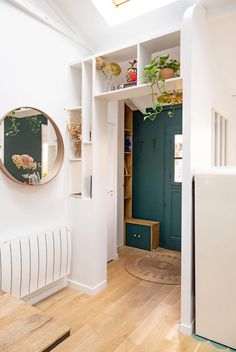 a room with white walls and wooden flooring next to a green cabinet filled with potted plants