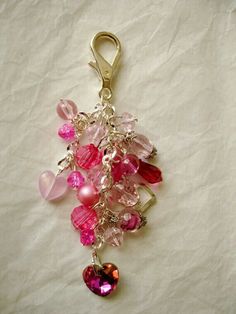 a bunch of pink and red glass beads hanging from a metal hook on a white sheet