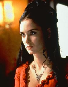 a woman with long dark hair wearing a red blouse and necklace, looking off to the side