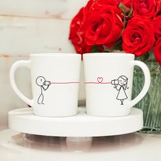 two coffee mugs with stick figures on them and red roses in the back ground