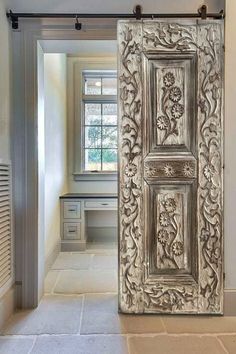 an ornate door is opened to reveal a room with white walls and tile flooring