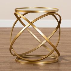 a gold metal table with a glass top on a wooden floor in front of a white wall