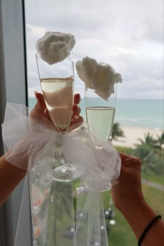 two champagne flutes being held up in front of a window with the ocean behind them