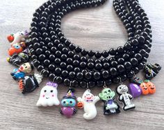 A fun and unique beaded charm statement necklace made with black acrylic beads and Halloween themed charms.  - Shortest strand measures 18.75- 20-75" - Charms measure approx. 1" long - Beads are 10mm - Lead free pewter connector  - Stainless steel lobster claw (or sterling silver)  - 2" Stainless steel extender chain The mannequin's neck size is 14.5".  We use the highest quality findings to ensure a piece that will last for years to come. DLD jewelry comes with a lifetime guarantee. This necklace is handmade in the USA. Dana LeBlanc Designs- Handmade Jewelry Black Themed Necklace For Halloween, Themed Black Necklace For Halloween, Halloween Themed Black Necklace, Halloween Black Jewelry With Charms, Black Halloween Jewelry With Charms, Adjustable Black Themed Necklace, Black Novelty Jewelry With Charms, Novelty Black Jewelry With Charms, Fun Black Round Beads Jewelry