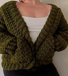 a woman is wearing a green knitted cardigan and white top with her hands in her pockets