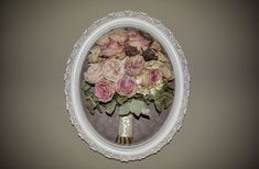 a bouquet of flowers in a white vase on a wall above a mirror with an oval frame