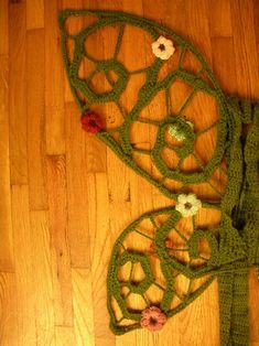 a green crocheted butterfly with flowers on it's wings sits on the floor