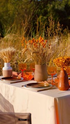 the table is set with plates, vases and flowers in front of an outdoor setting