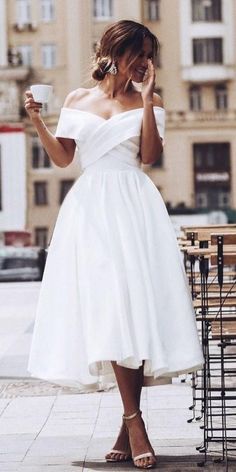 a woman in a white dress is holding a cup and talking on her cell phone