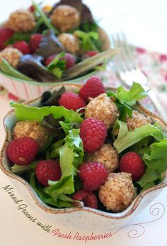 two bowls filled with raspberries and lettuce on top of a table