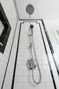 a shower head and hand shower in a white tiled bathroom with black and white tiling