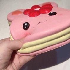 a hand holding a pink cake shaped like a pig with hearts on it's face