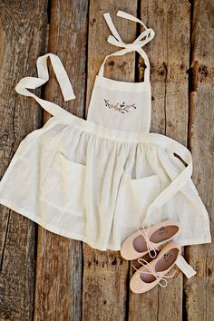 a white dress and sandals are sitting on a wooden floor next to a pair of shoes