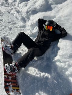 a snowboarder laying in the snow with his feet up on their board and wearing goggles