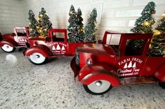 a red toy truck with christmas trees in the back and behind it on a granite countertop