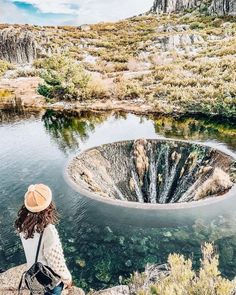 a woman sitting on top of a rock next to a lake with a large circular hole in it