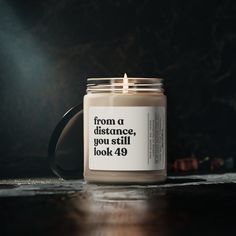 a candle sitting on top of a wooden table next to a black mug with the words from a distance, you still look 40