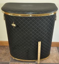 a black and gold trash can sitting on top of a tile floor next to a ruler