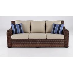 a wicker couch with blue and white pillows on it's backrests