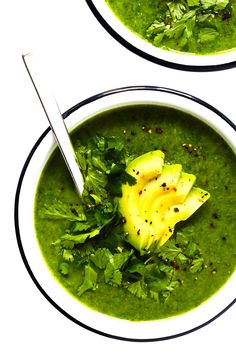 two bowls filled with green soup and topped with avocado