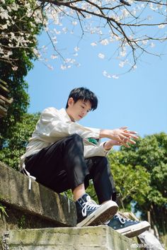 a young man sitting on top of a stone wall next to a tree with white flowers