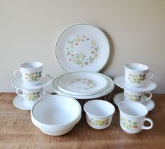 an assortment of white dishes and cups on a wooden table with a wall in the background