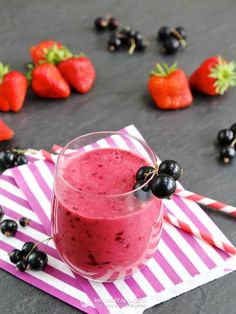 a smoothie in a glass with berries and strawberries next to it on a napkin