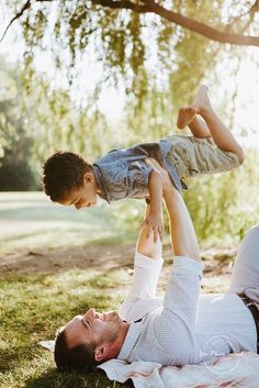 a father and son playing on the grass in front of a tree with their hands up