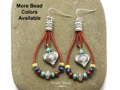 "Add a touch of bohemian flair to your accessory collection with these unique boho teardrop shaped leather earrings. The round leather cord is beautifully strung with your choice of seed bead colors, creating a vibrant and eye-catching look. A silver plated heart bead with a stunning southwestern design dangles elegantly in the center, adding a hint of charm to the overall design. Choose your preferred earring wires to personalize these stylish earrings to your liking. Perfect for adding a pop o Bohemian Adjustable Teardrop Earrings, Bohemian Teardrop Wire Wrapped Earrings, Multicolor Bohemian Teardrop Earrings, Bohemian Heart Jewelry For Everyday, Bohemian Earrings With Dangling Beads For Everyday, Handmade Brown Bohemian Teardrop Earrings, Bohemian Everyday Earrings With Dangling Beads, Adjustable Wire Wrapped Bohemian Teardrop Earrings, Bohemian Adjustable Wire Wrapped Teardrop Earrings