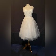 a white dress on a mannequin stand in front of a black background with the image of a woman's wedding dress