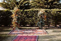 two rugs on the ground in front of some trees and bushes with orange flowers