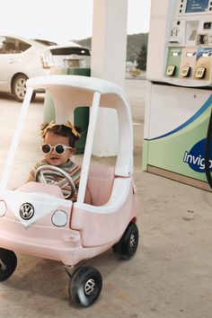 a small child in a pink toy car at a gas station with the hood up