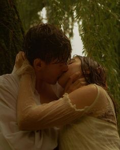 a man and woman kissing in front of some tall trees with their arms around each other